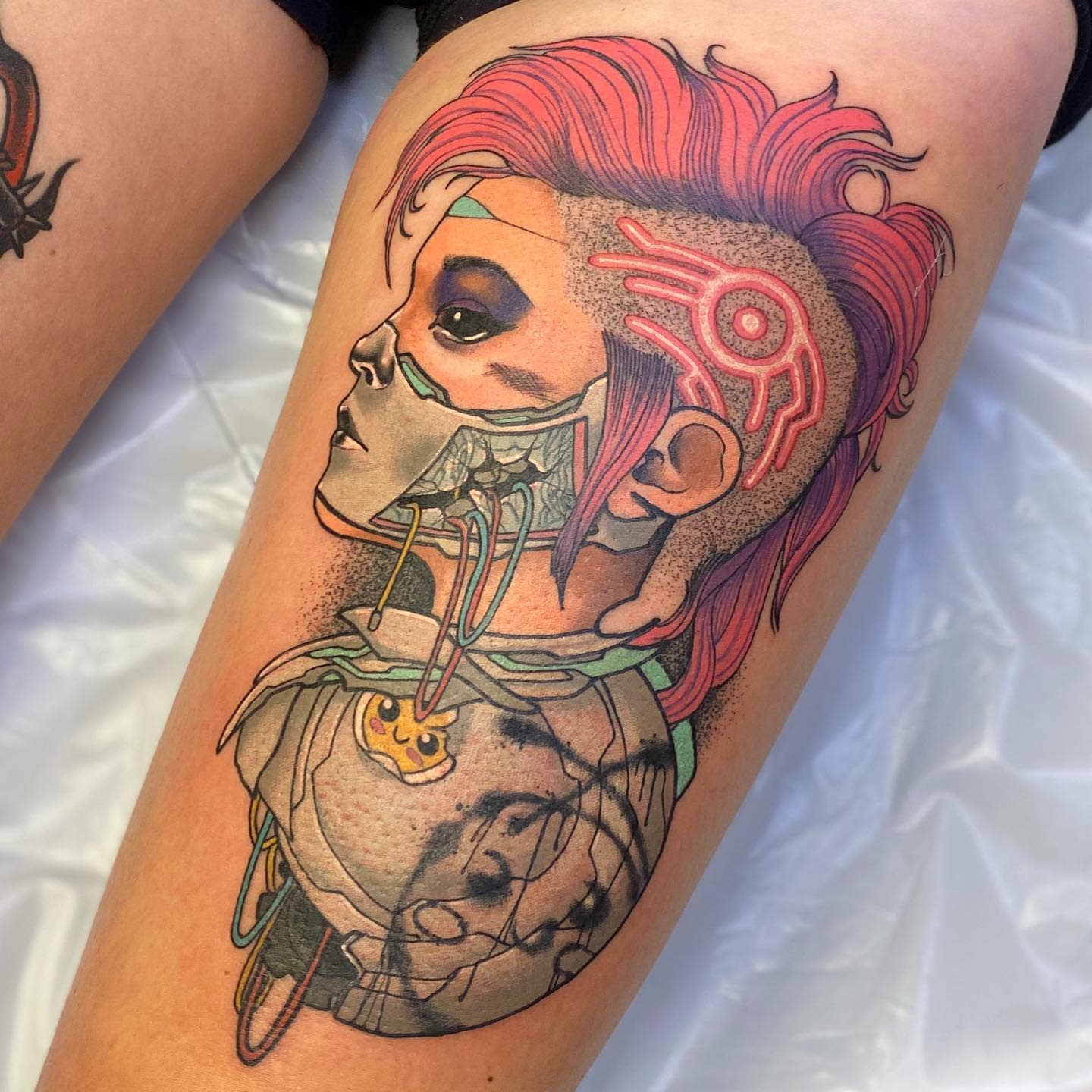 Vibrant cyberpunk tattoo on thigh featuring a profile of a female cyborg with pink hair, mechanical elements, and neon accents